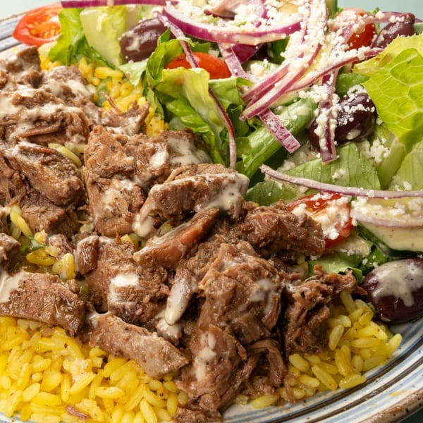 Mediterranean plate with gyro meat, yellow rice, and a fresh salad with feta and olives.