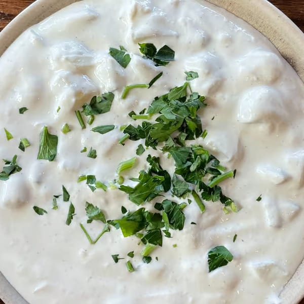 Close-up of a creamy white Mediterranean dish, possibly yogurt or sauce, garnished with fresh green parsley.
