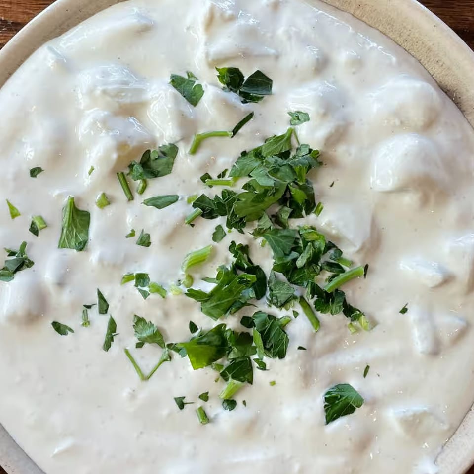 Close-up of a creamy white Mediterranean dish, possibly yogurt or sauce, garnished with fresh green parsley.